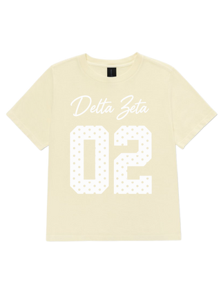 A pale yellow short-sleeve t-shirt with 'Delta Zeta' in white cursive and the number '02' in a white dotted pattern, displayed flat against a white background.