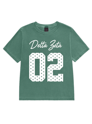 A green short-sleeve t-shirt with 'Delta Zeta' in white script and the number '02' in a white block font filled with small black dots, displayed on a solid white background.