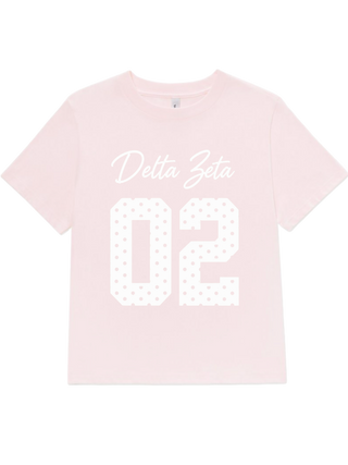 A light pink short-sleeve t-shirt with 'Delta Zeta' in white cursive script and the number '02' in a white dotted block font, displayed on a solid white background.